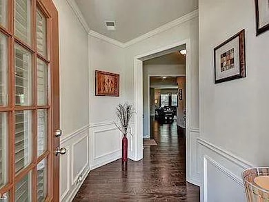 Hall with a decorative wall, crown molding, dark wood-type flooring, and wainscoting
