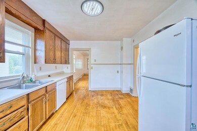 Kitchen with white appliances, a sink, light wood finished floors, light countertops, and brown cabinetry