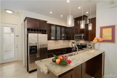 Kitchen with light tile flooring, hanging light fixtures, stainless steel appliances, light stone counters, and backsplash