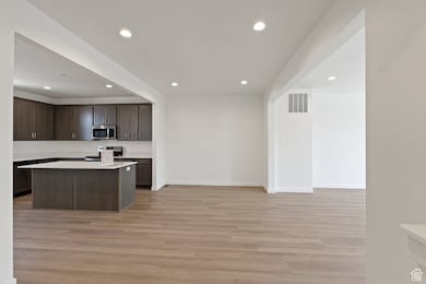 Kitchen featuring recessed lighting, dark brown cabinets, light countertops, light wood finished floors, and stainless steel microwave