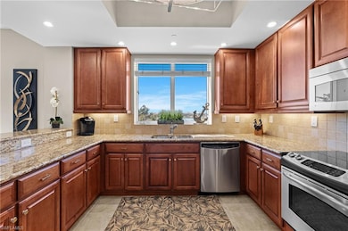 Kitchen featuring light stone counters, backsplash, appliances with stainless steel finishes, and a sink- Virtually Edited