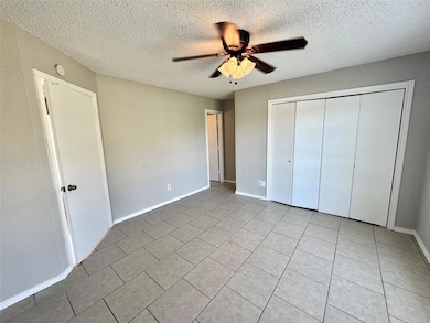 Unfurnished bedroom featuring a textured ceiling, light tile patterned flooring, ceiling fan, and a closet