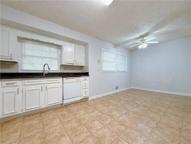 Kitchen with white dishwasher, a sink, ceiling fan, a textured ceiling, and white cabinetry