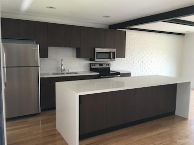 Kitchen with beam ceiling, appliances with stainless steel finishes, wood finished floors, and a sink