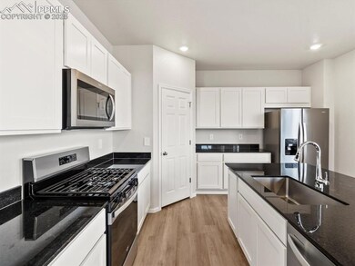 Kitchen featuring appliances with stainless steel finishes, dark stone counters, light wood-style flooring, white cabinetry, and recessed lighting