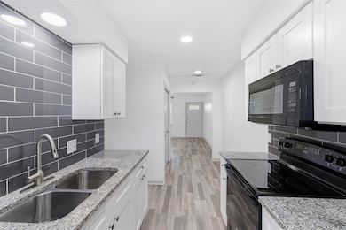 Kitchen featuring black appliances, decorative backsplash, white cabinets, recessed lighting, and light wood-style floors