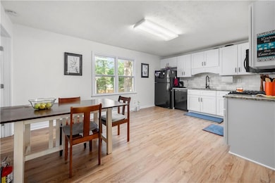 Kitchen featuring black appliances, light wood-type flooring, a sink, tasteful backsplash, and white cabinets