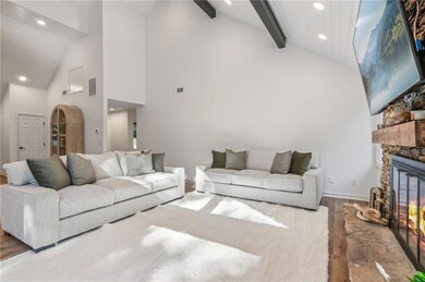 Living room featuring beam ceiling, a stone fireplace, high vaulted ceiling, and hardwood / wood-style floors