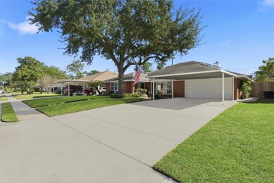This photo shows a charming single-story brick home with a well-maintained lawn and mature trees. It features a spacious driveway leading to a covered carport and garage. The neighborhood appears quiet and inviting, with sidewalks and neighboring homes visible.