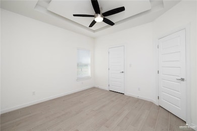 Spare room featuring a raised ceiling, baseboards, light wood-style flooring, and ceiling fan