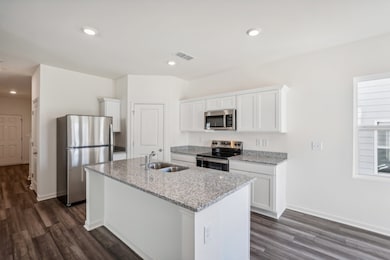 Kitchen featuring white cabinets, stainless steel appliances, light stone countertops, dark wood-style floors, and recessed lighting