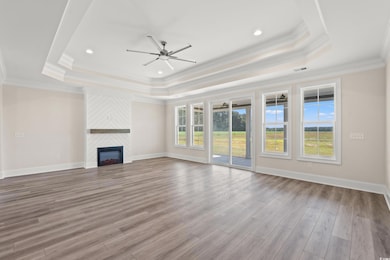 Unfurnished living room with a tray ceiling, ceiling fan, wood finished floors, ornamental molding, and a fireplace