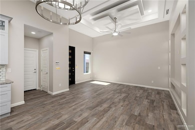 Unfurnished living room with dark wood-type flooring, recessed lighting, a ceiling fan, a chandelier, and a high ceiling