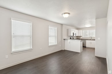 Kitchen with white cabinetry, dark wood-style flooring, healthy amount of natural light, dishwasher, and a textured ceiling