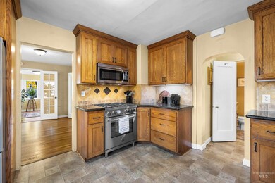 Kitchen featuring decorative backsplash, appliances with stainless steel finishes, arched walkways, stone finish floors, and brown cabinetry