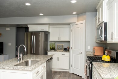 Kitchen with appliances with stainless steel finishes, light wood-type flooring, light stone counters, white cabinets, and recessed lighting