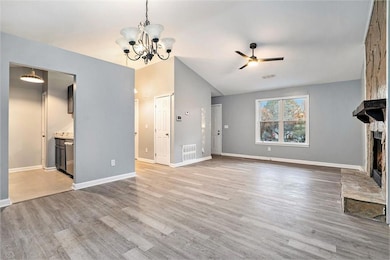 Unfurnished living room featuring ceiling fan, a fireplace, light wood finished floors, a chandelier, and vaulted ceiling
