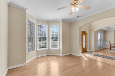 Foyer featuring arched walkways, light wood finished floors, crown molding, a ceiling fan, and baseboards