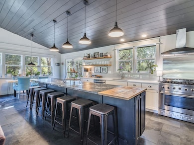 Kitchen featuring stainless steel appliances, lofted ceiling, decorative light fixtures, wall chimney range hood, and a kitchen bar
