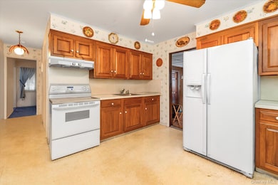 Kitchen with white appliances, light countertops, wallpapered walls, brown cabinetry, and a ceiling fan