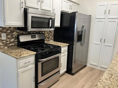 Kitchen with appliances with stainless steel finishes, light stone countertops, light wood-type flooring, white cabinetry, and backsplash