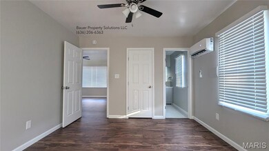 Unfurnished bedroom featuring dark wood-style floors, a wall mounted air conditioner, a ceiling fan, and ensuite bathroom