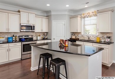 The open concept kitchen is overflowing with special features such staggered custom-like cabinets, oversize island, gem-like dark granite countertops, accented tile backsplash, recessed lighting, and music port with speakers.