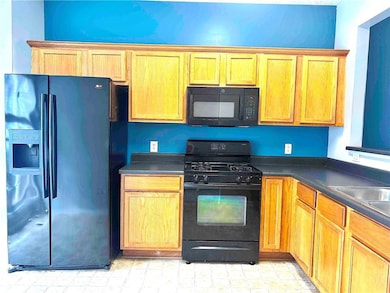 2nd view of kitchen featuring stained cabinets, black appliances and dark laminate countertops with vinyl patterned floors