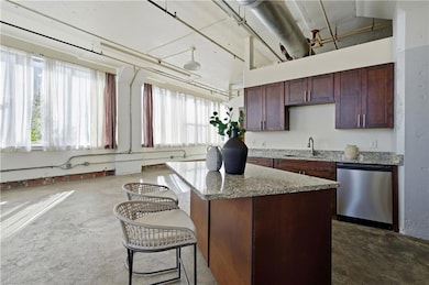 Kitchen with stainless steel dishwasher, a breakfast bar area, a center island, light stone counters, and dark brown cabinetry
