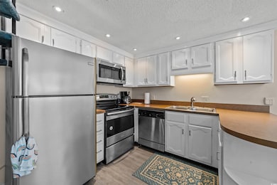 Kitchen featuring appliances with stainless steel finishes, a textured ceiling, recessed lighting, white cabinets, and light wood-style floors