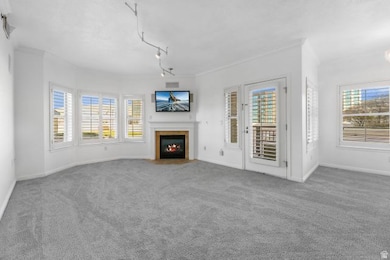 Unfurnished living room featuring carpet flooring, a fireplace with flush hearth, and crown molding