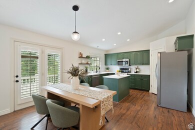 Kitchen with green cabinets, stainless steel appliances, open shelves, backsplash, and a center island
