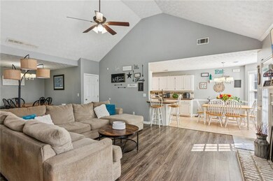 Living room with high vaulted ceiling, light wood-style flooring, a ceiling fan, and a chandelier