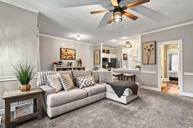Carpeted living room featuring crown molding, ceiling fan, baseboards, and a textured ceiling