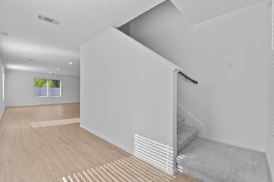 Bright, spacious interior with light wood flooring and neutral walls. Features a cozy carpeted staircase and large windows for natural light. Ideal for modern living.