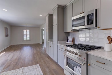 Kitchen featuring stainless steel appliances, gray cabinets, a chandelier, backsplash, and light wood-style flooring