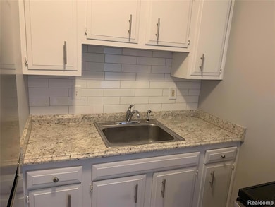 Kitchen with backsplash, white cabinets, and light stone countertops
