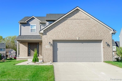 Traditional-style house featuring concrete driveway, covered porch, brick siding, a front yard, and a shingled roof
