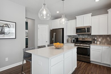 This spacious kitchen features a sizable pantry, a large island, quartz counters, recessed lighting, LVP wood floors, stainless appliances and more! (Photo of decorated model, actual home's finishes may vary slightly)