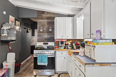 Kitchen featuring wooden walls, white cabinets, vaulted ceiling, dark hardwood / wood-style floors, and stainless steel range with gas stovetop
