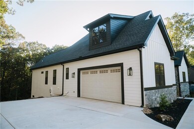 View of property exterior featuring roof with shingles, concrete driveway, stone siding, board and batten siding, and an attached garage