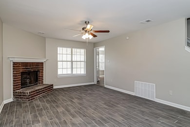 Unfurnished living room with a brick fireplace, dark wood-style flooring, and ceiling fan