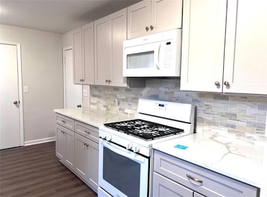 Kitchen featuring white appliances, light stone counters, dark wood-style floors, and backsplash