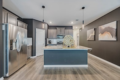 Kitchen with stainless steel appliances, decorative light fixtures, light stone countertops, light wood-style floors, and recessed lighting