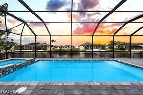 View of pool featuring glass enclosure, a pool with connected hot tub, a sunroom, and a patio