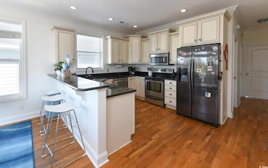 Kitchen with cream cabinetry, ornamental molding, appliances with stainless steel finishes, dark stone countertops, and a breakfast bar