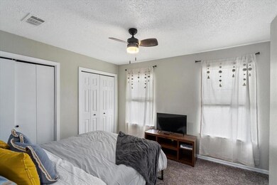 Carpeted bedroom with multiple closets, a textured ceiling, and a ceiling fan