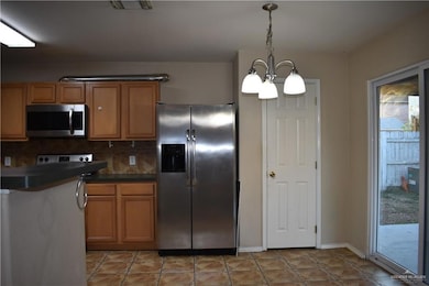 Kitchen with dark countertops, appliances with stainless steel finishes, brown cabinets, a chandelier, and backsplash