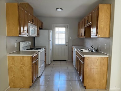 Kitchen featuring white appliances, a sink, light tile patterned floors, and light countertops