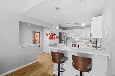 Kitchen with decorative backsplash, a breakfast bar area, white appliances, light wood finished floors, and white cabinets
